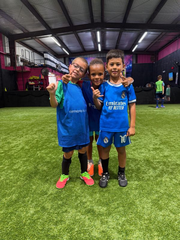 Three boys posing on an indoor soccer field.