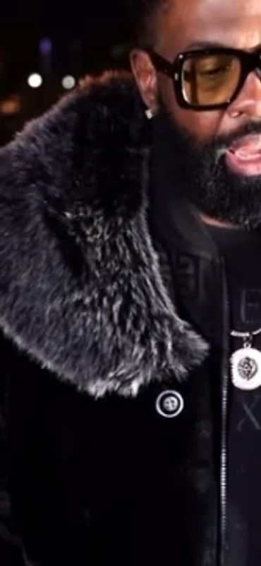 Man with fur coat singing into a microphone on a bridge at night.