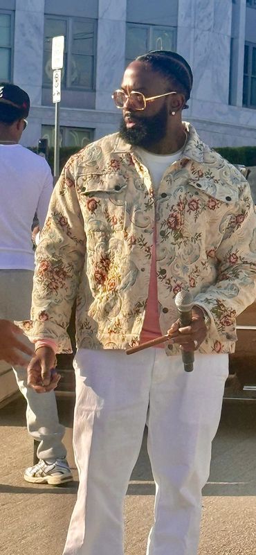 Man in floral jacket holding a microphone and drumstick outdoors.