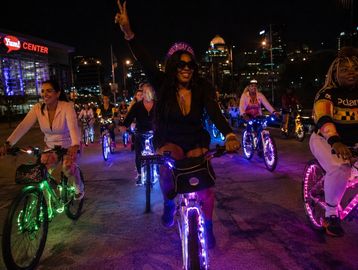 Group of people riding illuminated bicycles at night in a city.