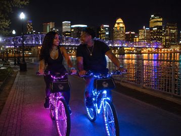 Couple riding illuminated bikes at night in city.