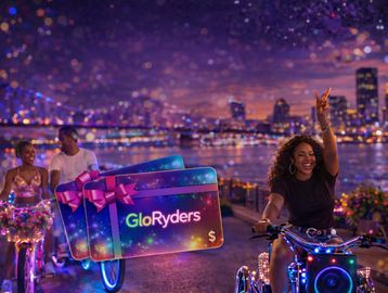 Woman rides a glowing bike at night with city lights in the background.