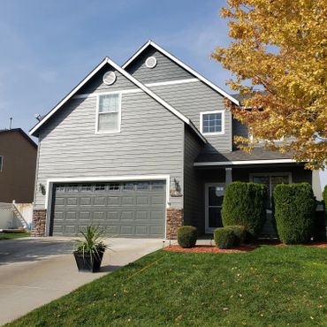 Gray two-story house with a garage and neatly trimmed bushes.