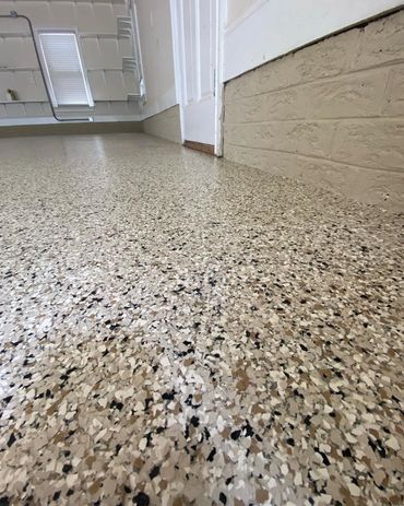 Close-up of a speckled epoxy floor in a room with white walls and a window.