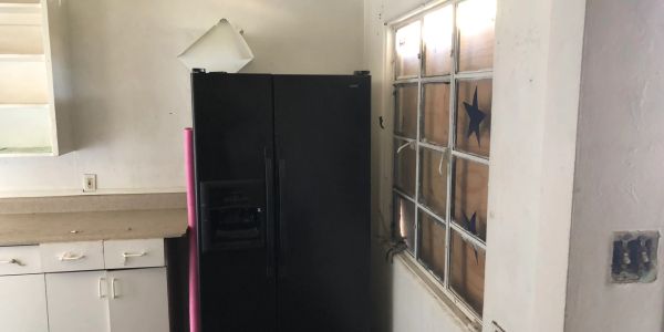 Black refrigerator next to a window and cabinets in a kitchen.