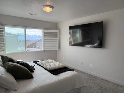 Modern bedroom with large window, wall-mounted TV, and a neatly made bed.