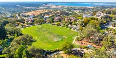 Aerial view of a green park surrounded by residential homes and overlooking a coastline.