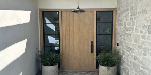 Modern wooden front door with side windows and plants.