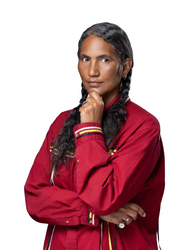 Confident person with braided hair wearing a red shirt, posing thoughtfully.