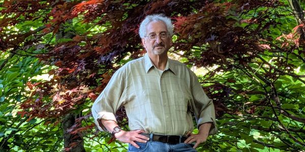 Man standing confidently in a garden with hands on hips.