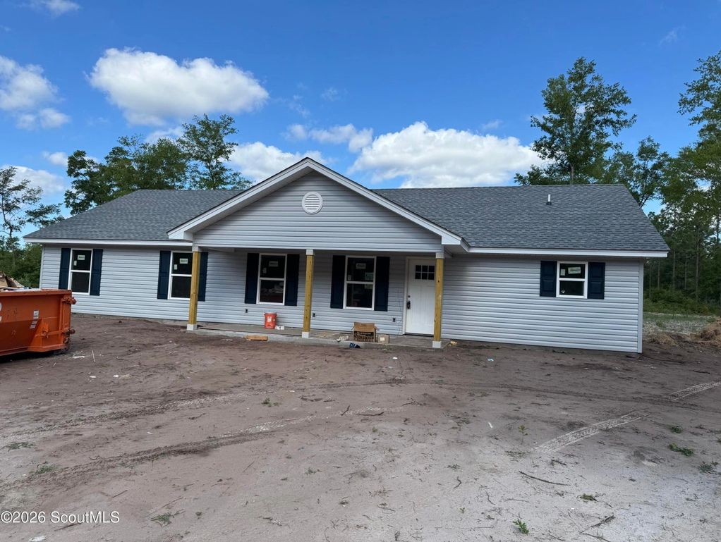 Newly constructed single-story house with gray siding and black shutters.