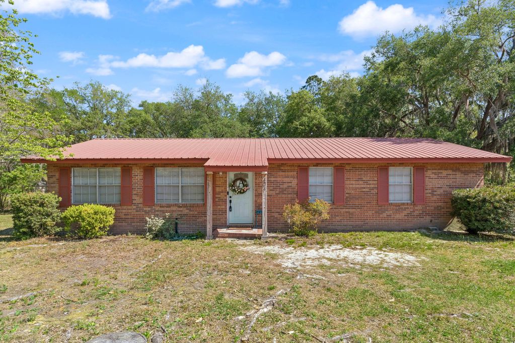 Single-story brick house with red shutters and a metal roof under a bright blue sky.