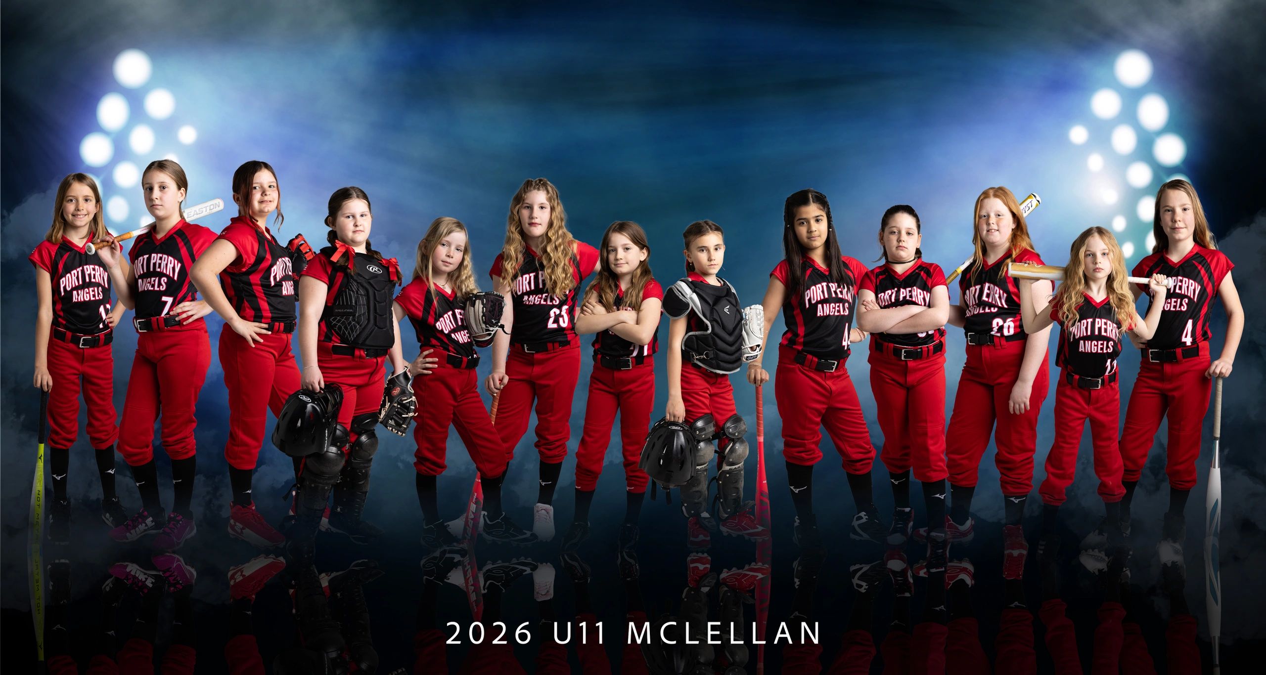 Youth softball team posing in red and black uniforms with bats and gloves under stadium lights.