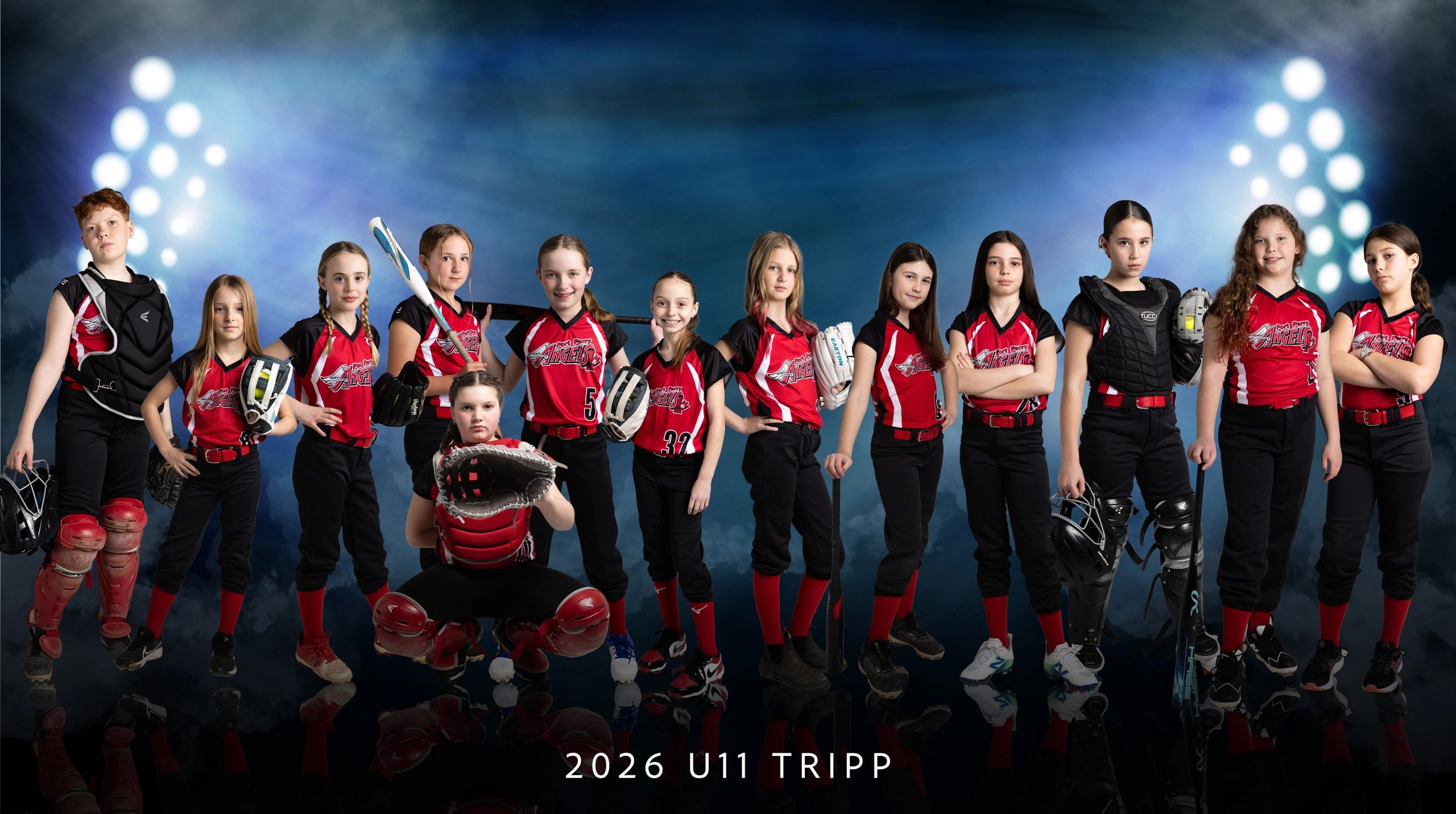 Youth softball team in red uniforms posing confidently under stadium lights.