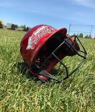 A red baseball helmet with a faceguard lying on grass.