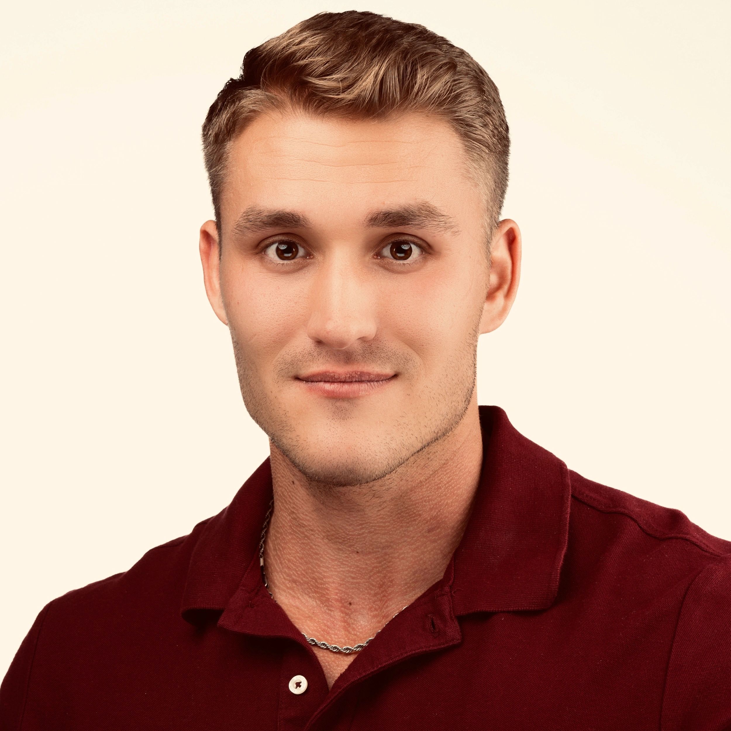 Close-up of a man in a maroon polo shirt with a silver chain necklace.