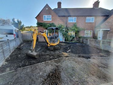 Mini excavator parked on freshly dug soil in front of a brick house.
