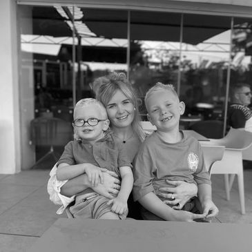 A woman smiles warmly with two young boys at an outdoor café.