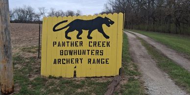 Yellow wooden sign for Panther Creek Bowhunters Archery Range beside a dirt road.