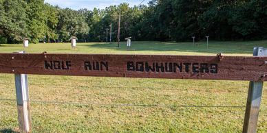 Wooden sign reading 'Wolf Run Bowhunters' in a grassy, wooded area.