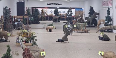 Indoor archery range with various 3D animal targets set up for practice.