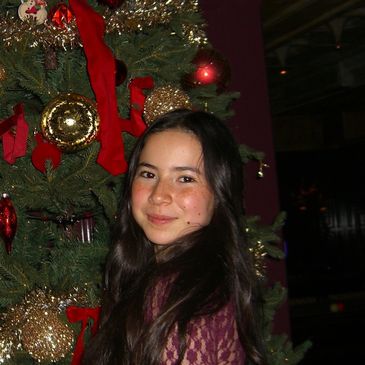Young woman smiling in front of a decorated Christmas tree.