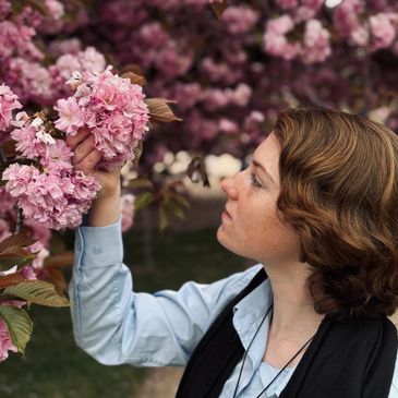 A woman admires pink cherry blossoms on a tree branch.