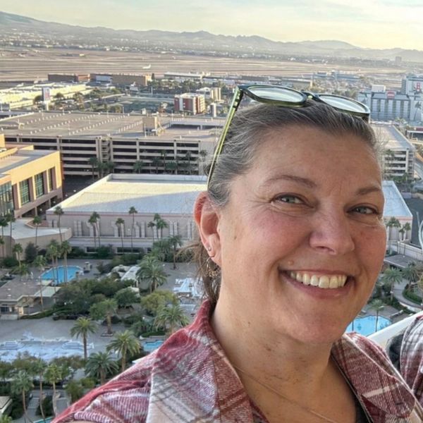 Woman smiling outdoors with a cityscape in the background.