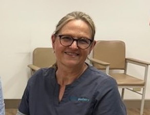 Smiling woman in glasses and scrubs sitting indoors.
