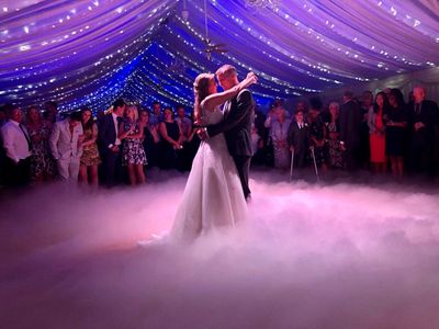 Bride and groom share a magical first dance surrounded by fog and guests.