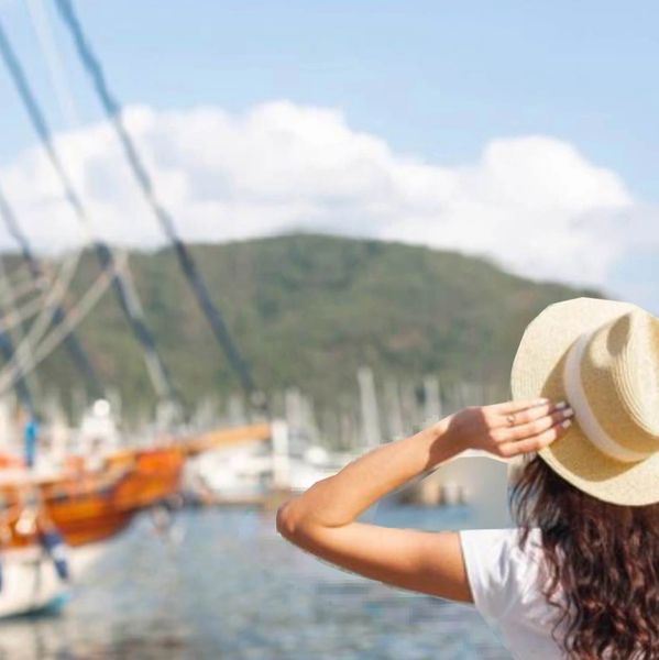 Woman in a hat enjoys a sunny day near boats and water.