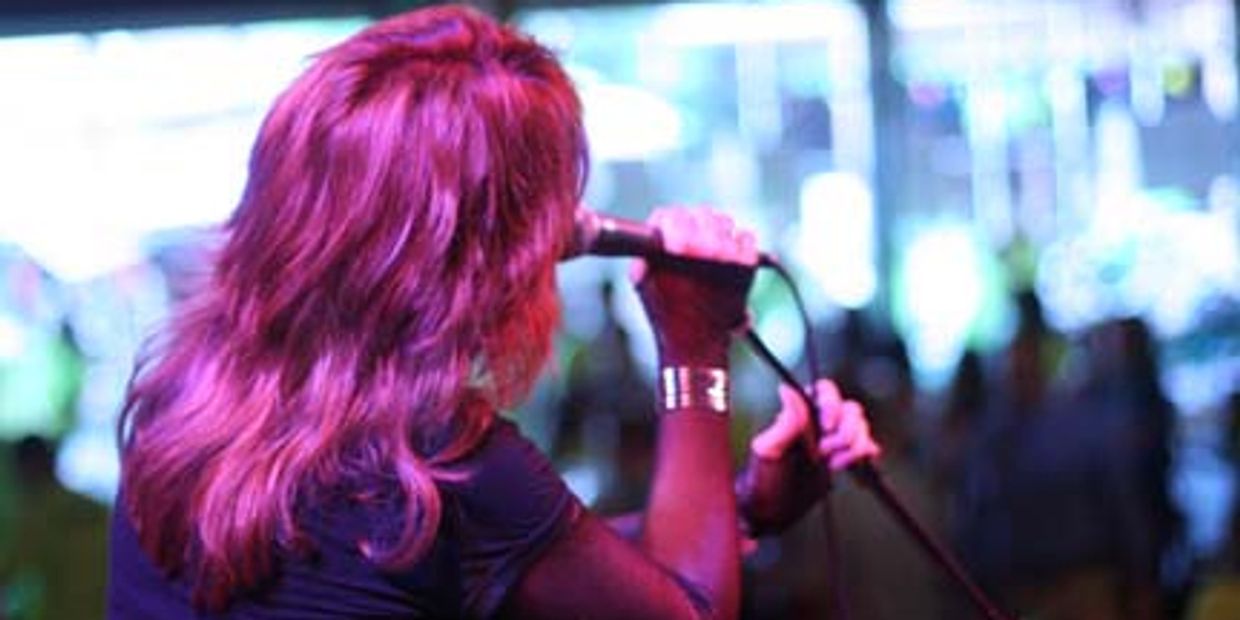 Person singing into a microphone on stage with vibrant lighting.