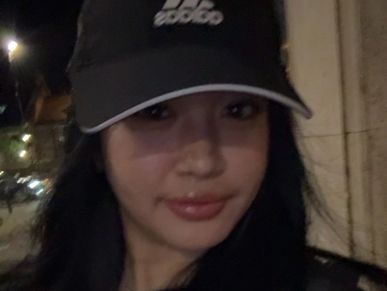 Young woman wearing a black Adidas cap at night.