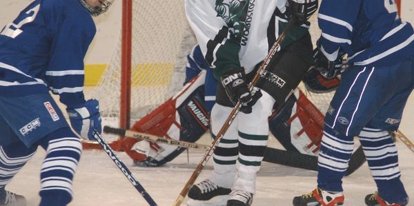 Youth ice hockey players battle near the goal crease during a game.