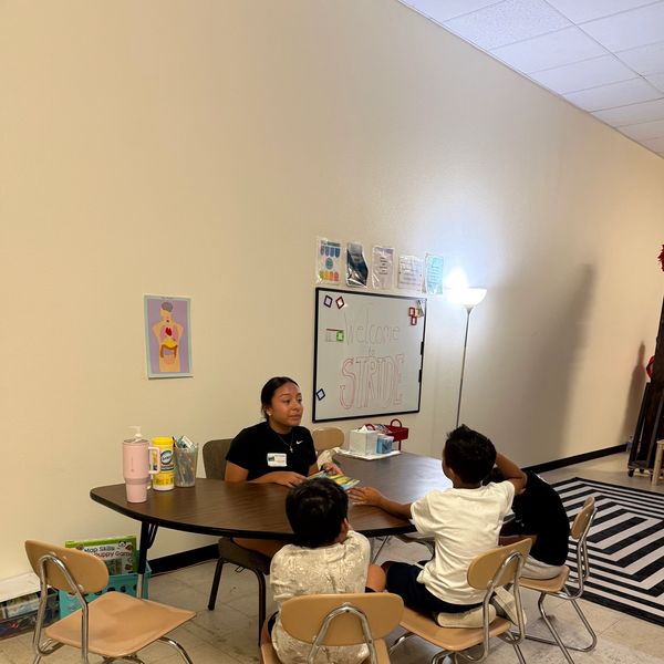 A woman talking to three children at a table in a classroom.