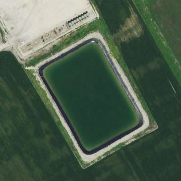 A large rectangular water reservoir in a green field.