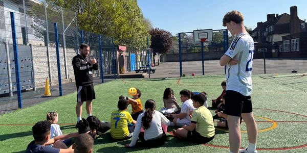 Coach instructs kids sitting on sports field on a sunny day.