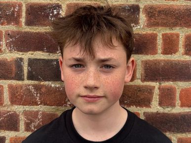 A young boy with freckles standing against a brick wall.