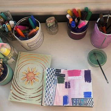 Art supplies and journals arranged on a workspace desk.