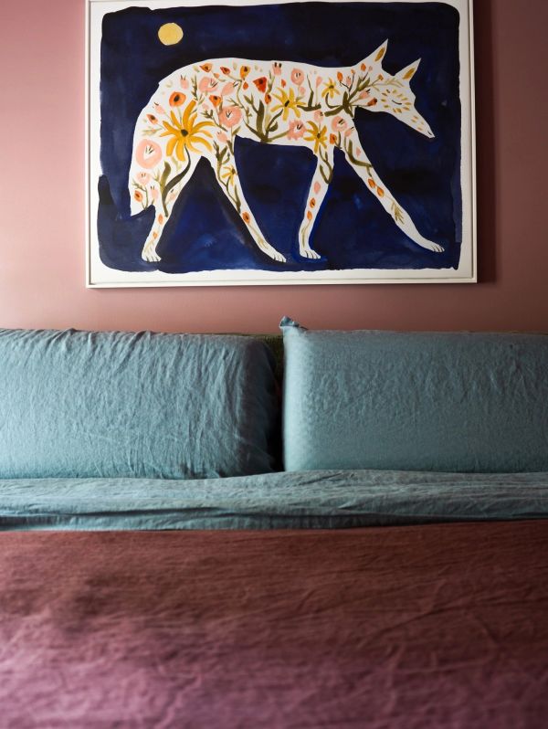Artistic floral dog painting above a blue sofa and brown bedspread.