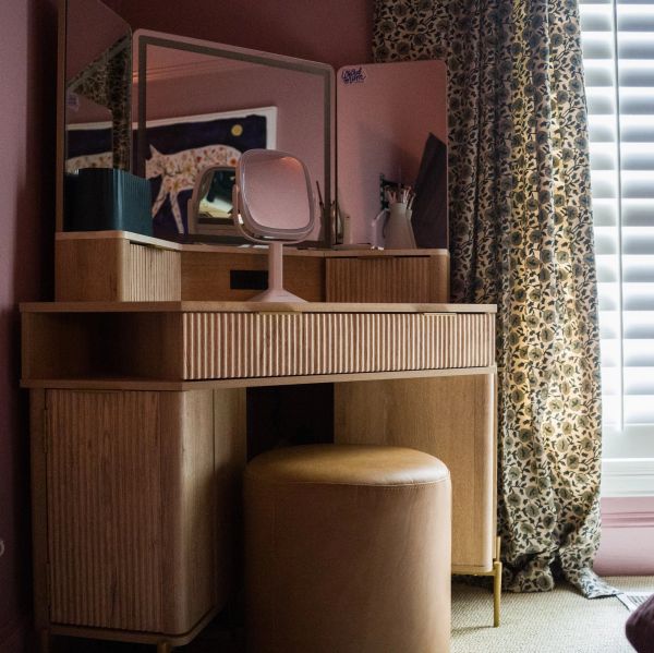 Wooden vanity with a round leather stool and animal print curtain in soft lighting.