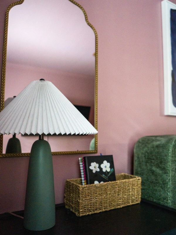A modern green lamp with a pleated white shade on a black surface.