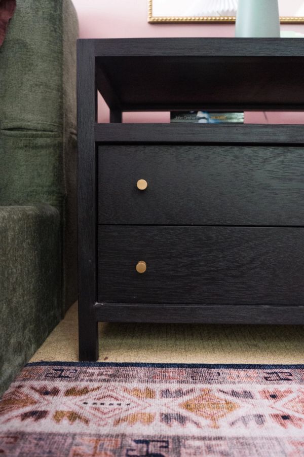Close-up of a dark wooden nightstand with gold knobs next to a green sofa.