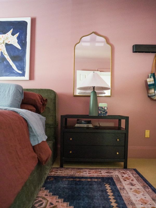 Cozy bedroom corner with a green bed, dark nightstand, and decorative mirror.