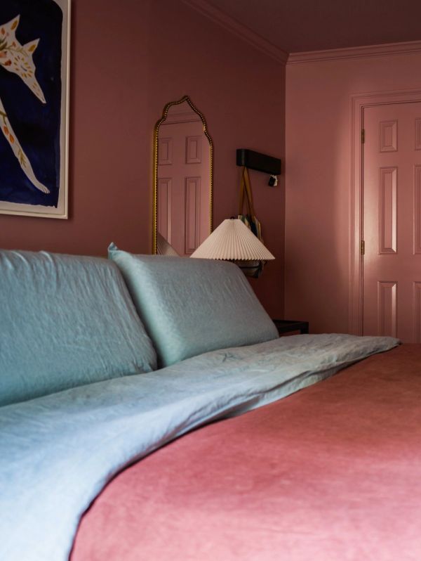 Cozy bedroom with pastel bedding and a vintage mirror on a muted pink wall.