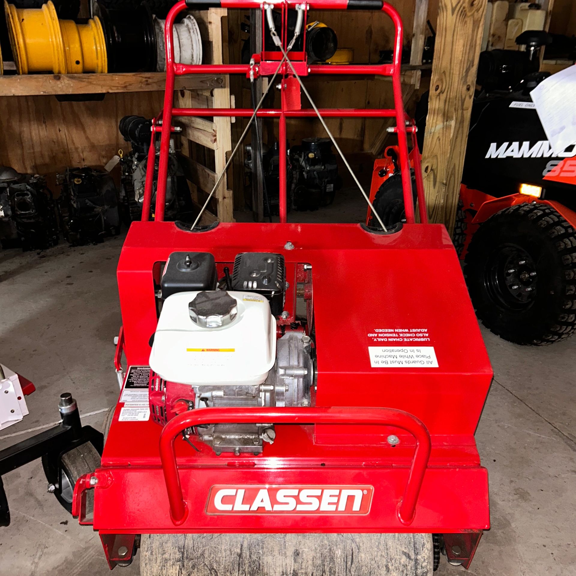 Red Classen lawn roller with a white engine in a workshop.