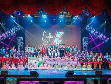 Large group of performers posing on stage under Electric Lightning sign.