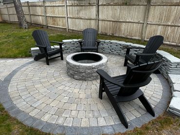 View of newly installed wood firepit and four black comfortable adirondack chairs
