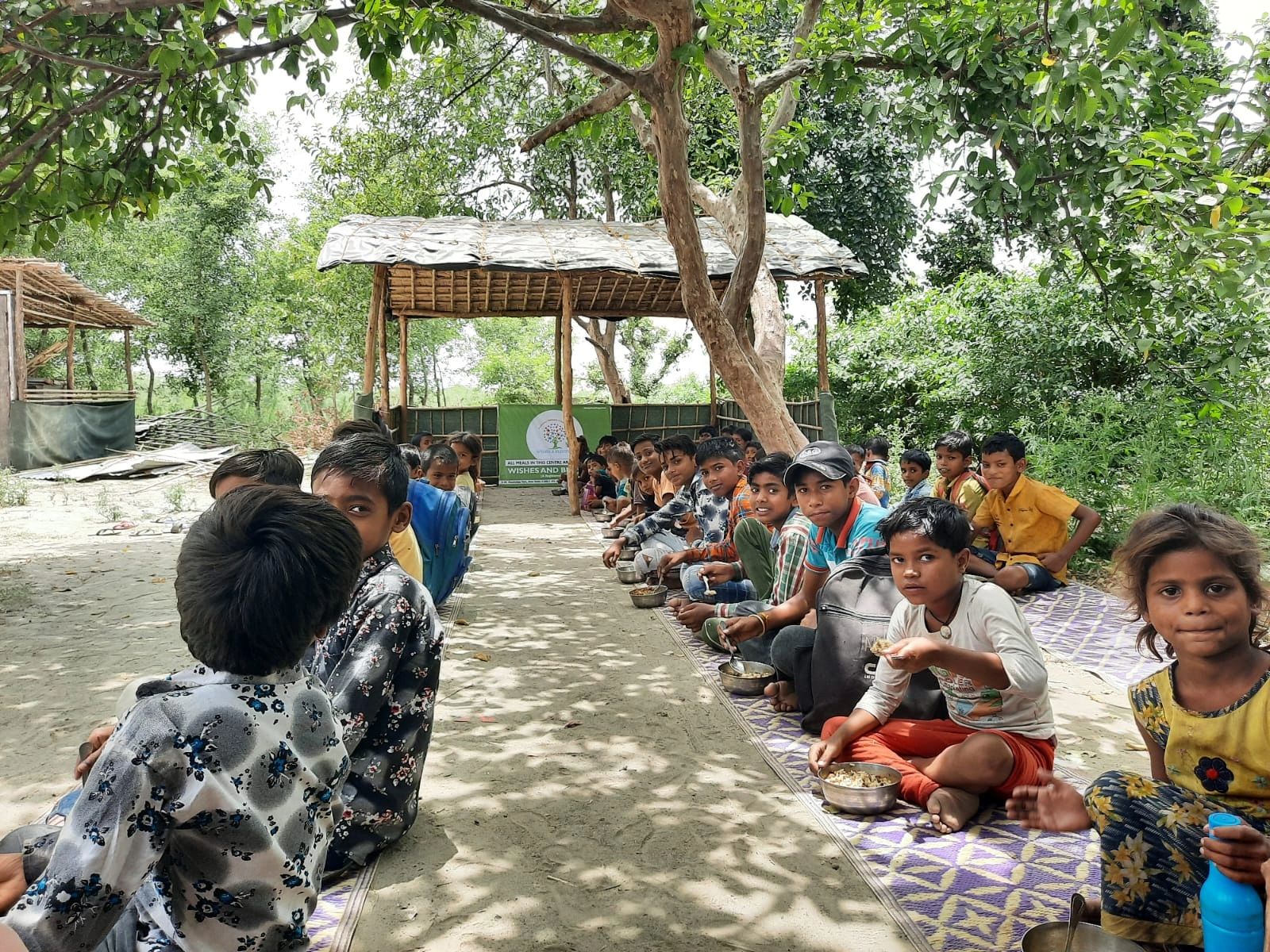 Children eating together outdoors under a shaded area.