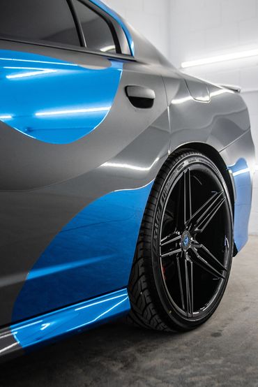 Close-up of a sleek blue and gray sports car rear with black alloy wheel.